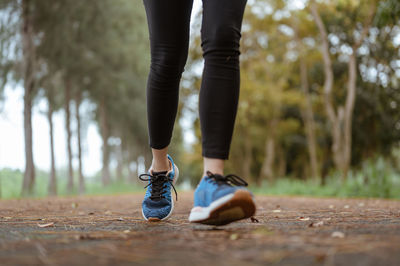 Low section of woman running on road amidst forest