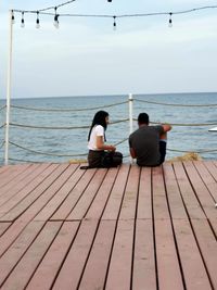 Rear view of people sitting on sea against sky