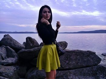 Young woman standing on rock at sea shore against sky