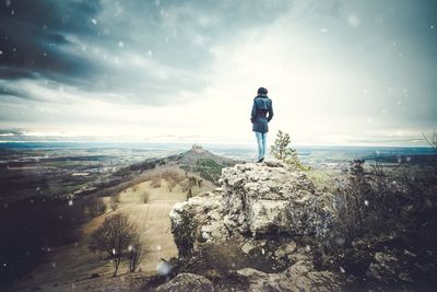 Rear view of woman standing on cliff against cloudy sky during snowfall