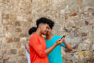 Happy young woman using mobile phone against brick wall