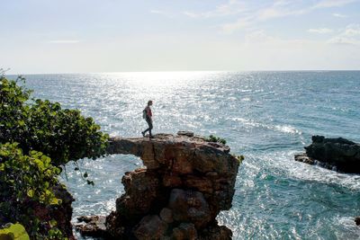 Woman hiking on rock formation over sea against sky at puente de piedra