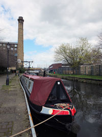 Boat moored on canal by building against sky