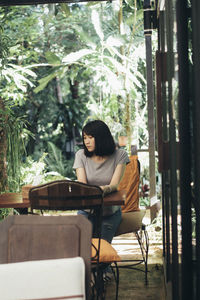 Woman sitting on chair against trees