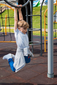 Full length of boy hanging on monkey bars in playground