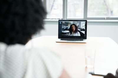 Rear view of businesswoman discussing with female colleague over video conference in board room