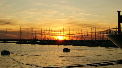 Sailboats moored on sea against sky during sunset