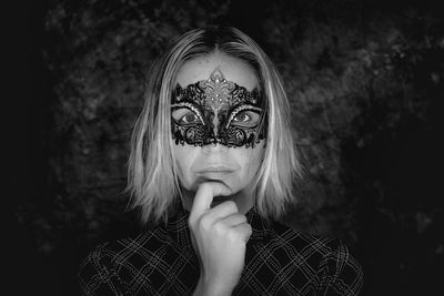 Close-up portrait of young woman wearing masquerade mask against wall