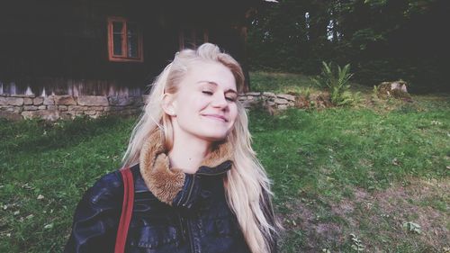 Happy young woman with blond long hair standing in yard