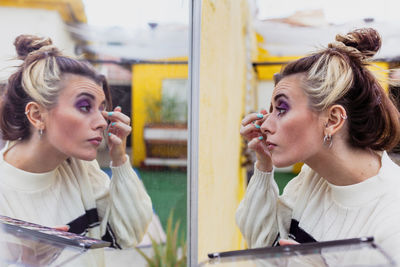 Young woman applying eye shadow looking at mirror while standing in back yard