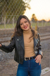 Portrait of smiling young woman standing against fence