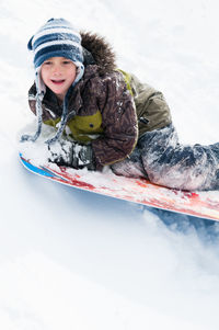 Cute boy tobogganing on snow covered land