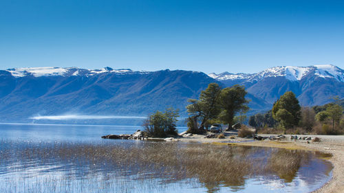 Scenic view of lake and mountains against clear blue sky