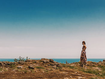 Woman standing on cliff by sea against clear sky