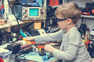 Side view of boy repairing equipment on table in workshop