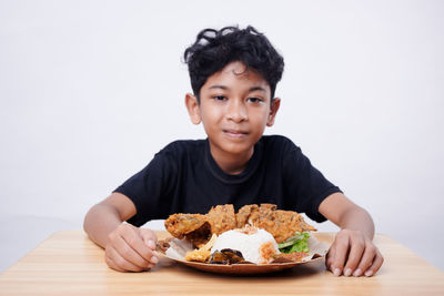 Portrait of cute girl eating food on table against white background