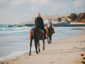 Young man riding horse on beach against sky