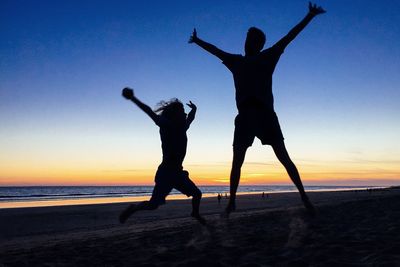 Silhouette friends jumping at beach against sky during sunset