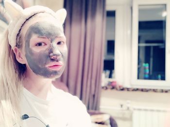 Close-up portrait of young woman with face mask sitting at home