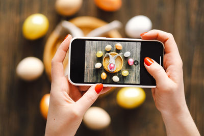 Woman holding mobile phone and making photo of eggs painted for easter isolated on wooden background