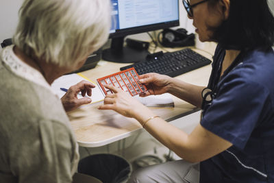Female doctor discussing over pill organizer with senior patient sitting at desk in office