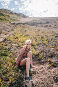 Smiling young woman sitting on field against sky