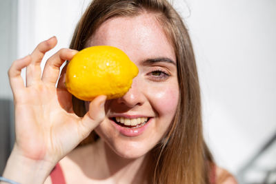 Portrait of smiling young woman holding lemon against wall