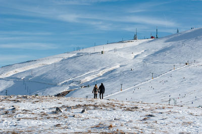 Rear view of people on snow covered landscape against sky