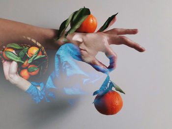 Double exposure portrait of a woman and hand holding tangerine fruit against white background