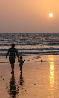 Silhouettes of people walking on beach during sunset