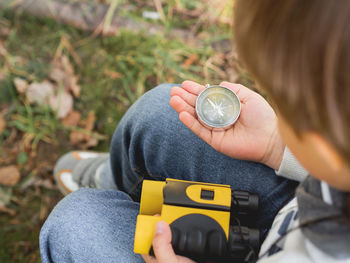 Little explorer on hike in forest. boy with binoculars and compass sits on stump and reads map.