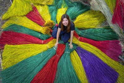 High angle portrait of smiling woman sitting on multi colored straws outdoors