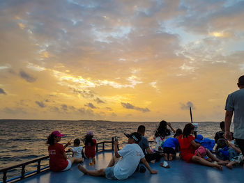 People sitting by sea against sky during sunset