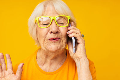 Close-up of senior woman talking on phone against yellow background