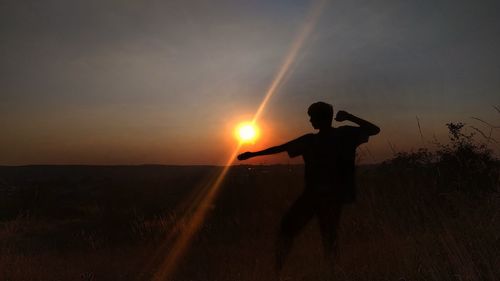 Silhouette teenage boy standing on land against sky during sunset