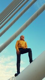 Low angle view of girl standing on bridge against blue sky