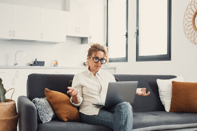 Young woman using phone while sitting on sofa at home