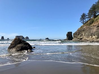 Rock formation in sea against clear blue sky