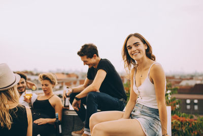 Smiling young woman sitting with friends at rooftop party