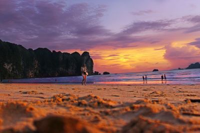 Woman walking at beach against sky during sunset