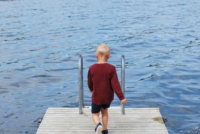 Rear view of boy standing on pier over lake