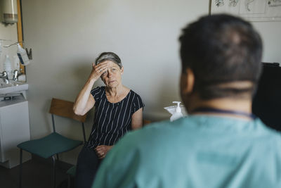 Senior woman touching forehead while discussing with doctor in clinic