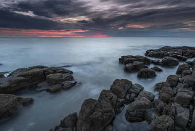 Rocks by sea against sky during sunset