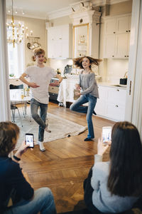 Friends photographing teenage boy and girl dancing at home