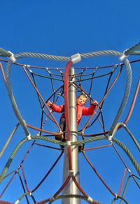Low angle view of boy on play equipment against clear blue sky