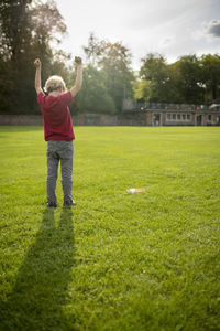Rear view of boy with arms raised standing on grassy field