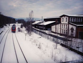 Train on snow covered railroad tracks against sky during winter