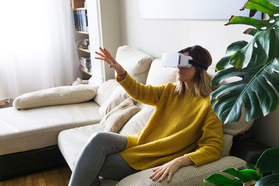 Young woman using virtual reality simulator on sofa at home