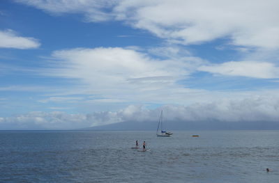 People paddle boarding in sea against sky