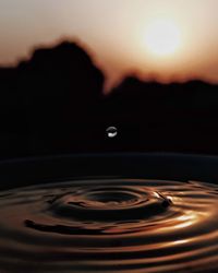 Close-up of drop falling on water at sunset